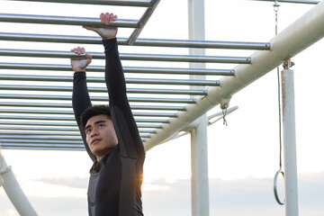 Young asian fit man climbing monkey bars outdoors in boot camp
