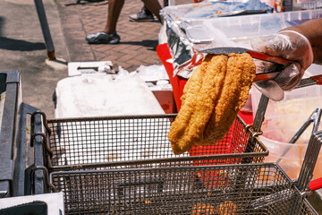 Gloved Hand Holding a Crispy Golden Fried Catfish Filet over a Metal Basket and Fryer at an Outdoor...