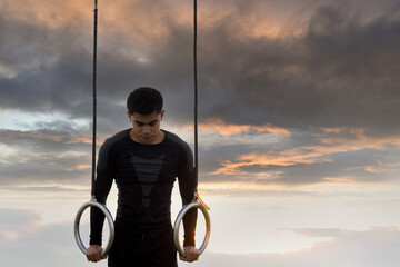 Muscle-up exercise young man doing intense workout at outdoor gym on gymnastic rings