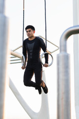 Young man exercising in an outdoor bodybuilding gym using gymnastic rings