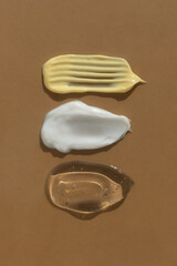 Smears of yellow, white cream and transparent gel or serum on a brown background. The texture of a cosmetic skin care product. Top view.