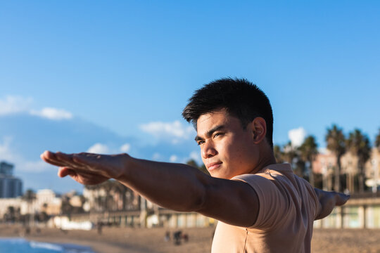 Focus Asian man standing in yoga tree pose on ocean beach at sunset, relax holiday vacation time at tropical beach
