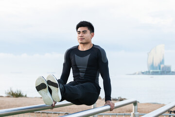 Young Asian man exercising on parallel bars outdoors