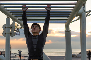 Muscular Asian man exercising on calisthenics bars