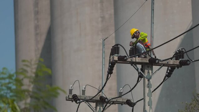 A man in a yellow helmet is working on a power line. Concept of danger and risk, as the man is working at a height and is exposed to potential hazards