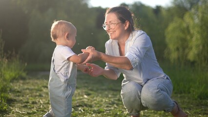 mom hugging baby son in nature. happy family kid dream concept. baby goes to mom in nature in the...