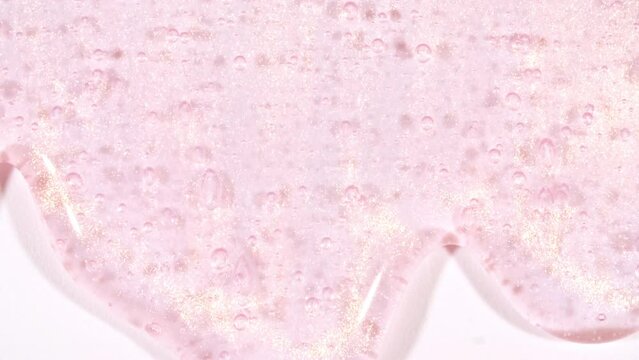 Pink Transparent Cosmetic Gel Fluid With Molecule Bubbles Flowing On The White Surface. Macro Shot. Liquid Cream Gel Transparent Cosmetic Sample Texture With Bubbles. High quality 4k footage