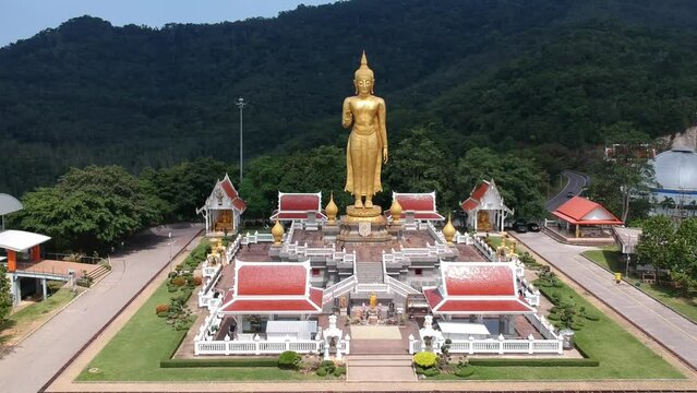Aerial drone view of giant golden  Buddha statue Phra Buddha Mongkol Maharaj above Buddhist temple complex with mountain forest background, Hat Yai, Songkhla, Thailand