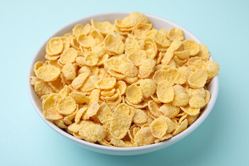 Breakfast cereal. Tasty corn flakes in bowl on light blue table, closeup