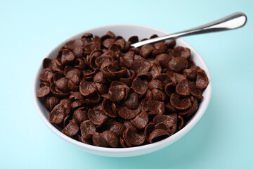 Breakfast cereal. Chocolate corn flakes in bowl and spoon on light blue table, closeup