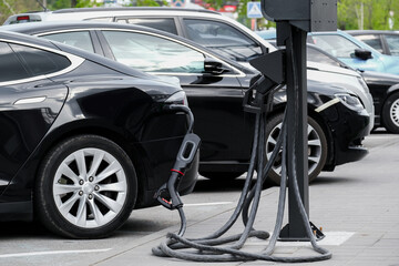 A line of electric cars with alloy wheels is getting charged in a parking lot. Electric cars are charged with ecological renewable energy. - obrazy, fototapety, plakaty