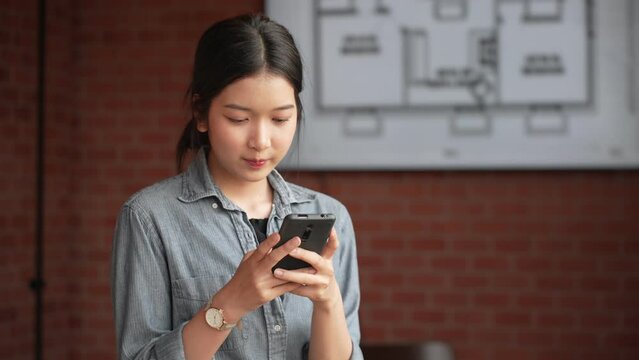 The young Asian female architect is using her smartphone to discuss work matters at her office