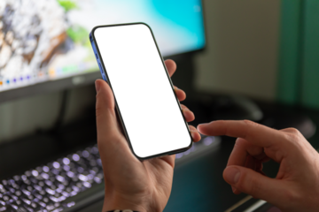 A man is using a smartphone with a blank, frameless screen against the background of a computer monitor.
