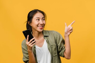 Portrait Young Asian Lady Using Mobile Phone With Cheerful Expression Show Something Amazing Blank Space Casual Clothing Stand Isolated Yellow Wall Facial Expression Concept