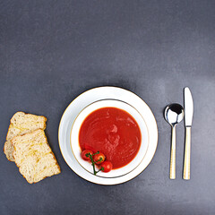 Tomato, soup and bread on menu in restaurant with bowl of healthy food, spoon and knife on table. Dinner, dish or luxury appetizer course in fine dining kitchen with vegetables for nutrition in diet