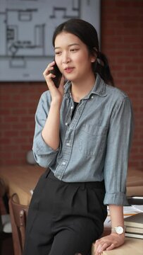 The young Asian female architect is using her smartphone to make work-related calls at her office