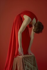 Woman in red dress bending over piece of cloth on red background in elegant fashion concept