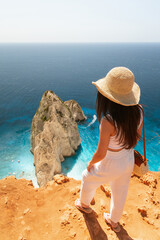 A young girl stands on the edge of a cliff and looks at the blue sea.