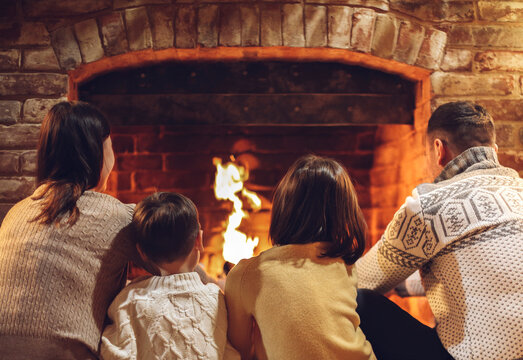 Happy young family parents with two small kids gathering around brick fireplace in cozy and warm country house during Christmas holidays