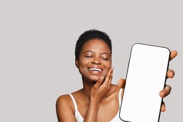 Enjoying healthy woman holding smartphone with white empty blank screen display on gray studio wall...