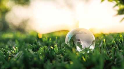 Glass crystal globe on the green grass nature in sunset, concept for environment and conservation