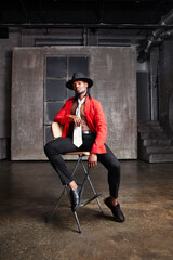 Fototapeta na wymiar Contemporary African American man, actor or dancer sits on a stool on stage, dressed in a red shirt and a hat