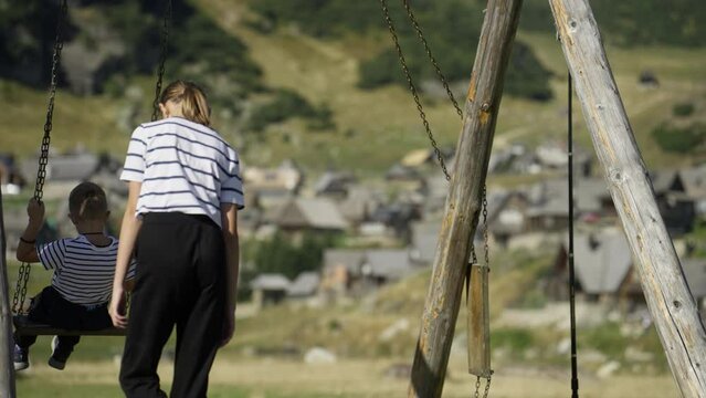 Sister Pushing Brother on a Swing Nearby Mountain Village. Concet of Bonding, Siblings' Help, Childhood Fun
