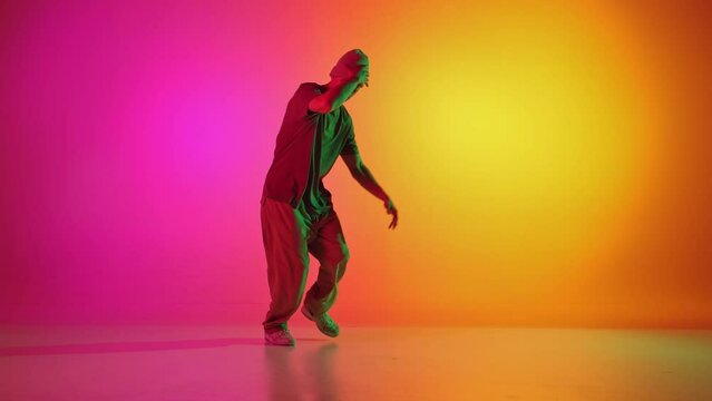 Young man dressed sportswear and dancing in motion in neon light against gradient pink-yellow background. Concept of hobby, sport, creativity, fashion and style, motion, action. Ad