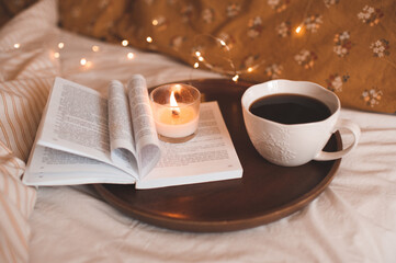 Cup of coffee with open paper book with folded pages in heart shape and burning scented candle over...