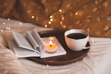 Cup of coffee with open paper book with folded pages in heart shape and burning scented candle over glowing lights close up.