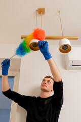 in the apartment cleaner in a yellow apron is cleaning a chandelier with a dust brush