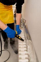close up top shot in an apartment cleaner in a yellow apron washes a white radiator with a steam generator