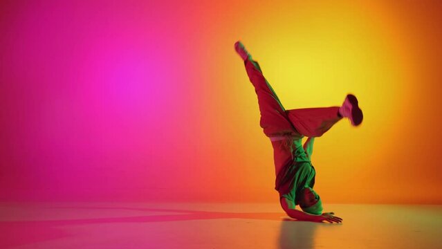 Young, stylish dressed man dancing in vibrant neon light against gradient pink-yellow background. Breakdance. Concept of hobby, sport, creativity, fashion and style, motion, action. Ad