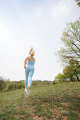 An athletic girl performs a jog in the park. Beautiful blonde Caucasian woman in blue tight...