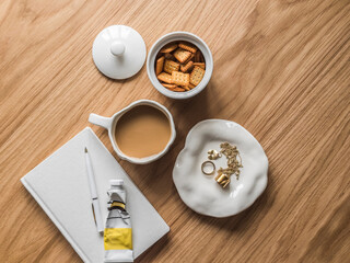 Tea break - a cup of tea with milk, crackers, notepad, hand cream, decorations on a wooden table, top view