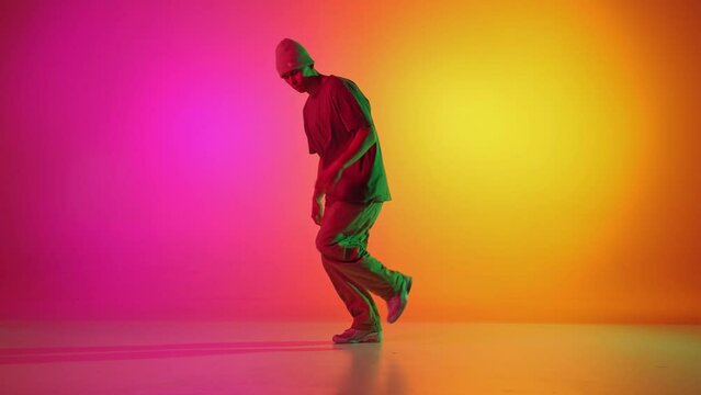 Self-expression through moves. Contemporary dancer dancing in motion in neon light against gradient pink-yellow background. Concept of art, hobby, sport, creativity, fashion and style, action. Ad
