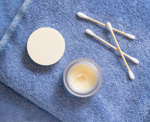 Opened lip balm jar with blank lid near cotton swabs on folded blue towels, mockup