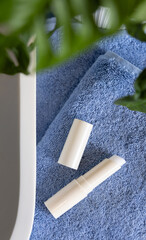 Opened lip balm on blue towels near basin and green monstera in bath, lid mockup