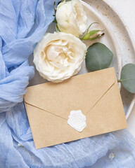 Envelope near blue tulle fabric knot and cream roses on plates top view copy space, wedding mockup