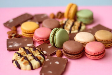 Pastel macarons, almond chocolate, peanut butter cookies and various nuts on bright pink background. Selective focus.