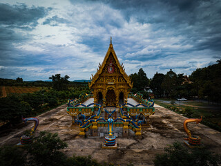 Chachoengsao, Thailand, 28 July 2023. Wat Khao Tham Raet, Temple with a weathered stone exterior, surrounded by statues of snakes. The sky is overcast with dark clouds.