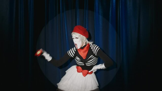 Hilarious female mime artist showing weightlifting exercises with flower toy while standing on stage in spotlight and performing improvised comedy