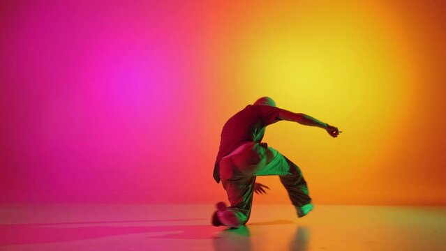 Talented solo artist, male break-dancer performing hip-hop in neon light against gradient pink-yellow background. Concept of art, hobby, sport, creativity, fashion and style, action. Ad