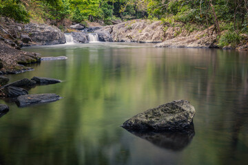 A pond of smooth reflecting water surrounded by rocks, rainforest, with two little waterfalls...