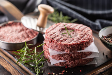 Fresh raw ground beef patties with rosemary salt and pepper made in a meat form on a cutting board - 786375355