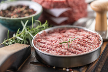 Fresh raw ground beef patties with rosemary salt and pepper made in a meat form on a cutting board - 786375908