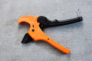 An orange and black pipe cutter lies on concrete surface.