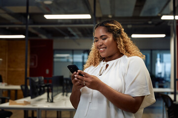 Young multiracial woman in businesswear smiling and using mobile phone in office