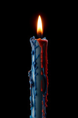 Candle with red and blue wax burning on black background