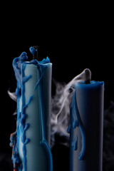 Blue candles in melted wax with smoke on black background